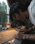 Rio Kaneki leaned over a wooden carving creating a stencil for his screen printing