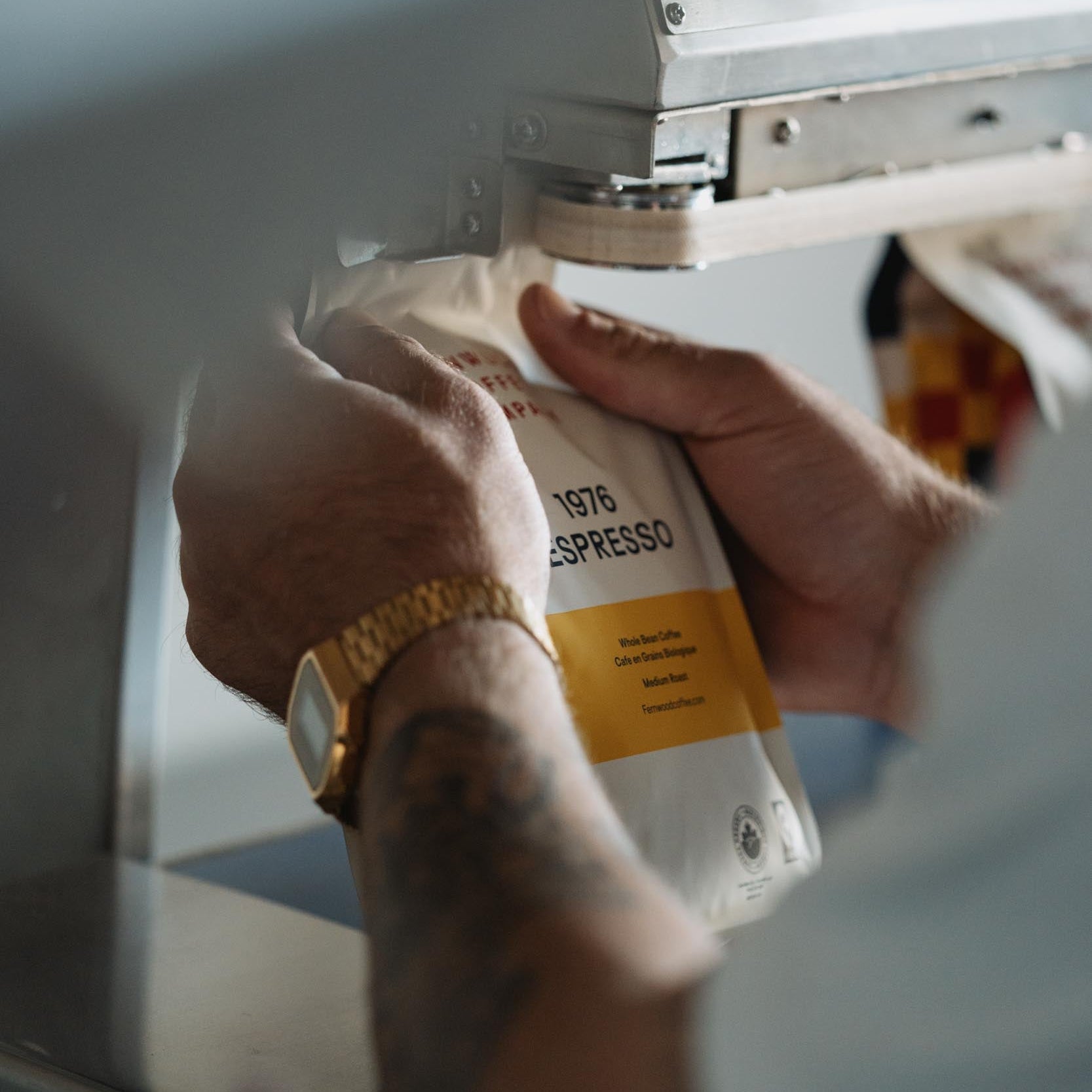 A person holding a bag of 1976 Espresso passing it through a bag sealer at the roastery.