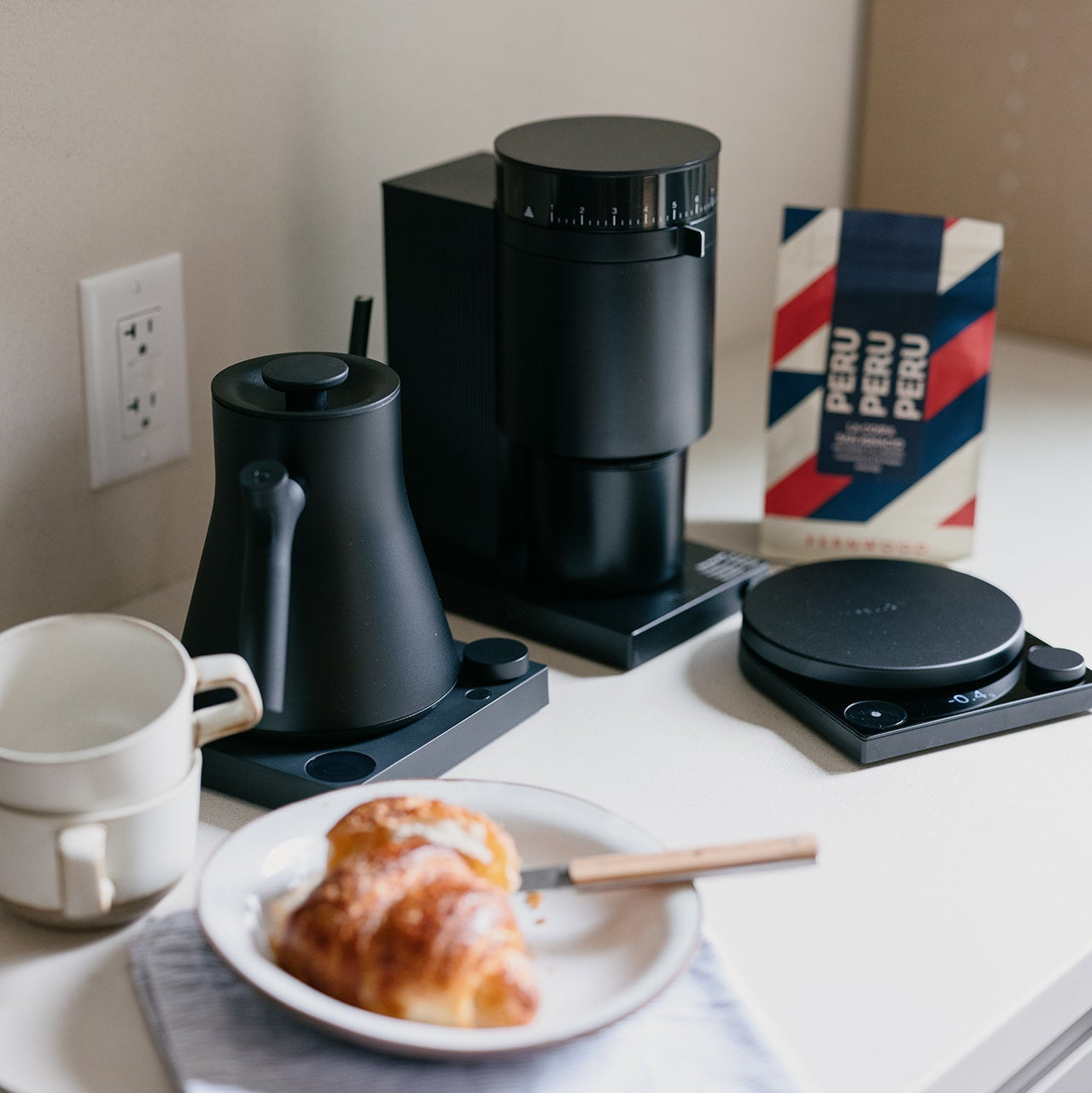 Black coffee maker on a kitchen counter with a plate of food and a Peru coffee bag in the background.
