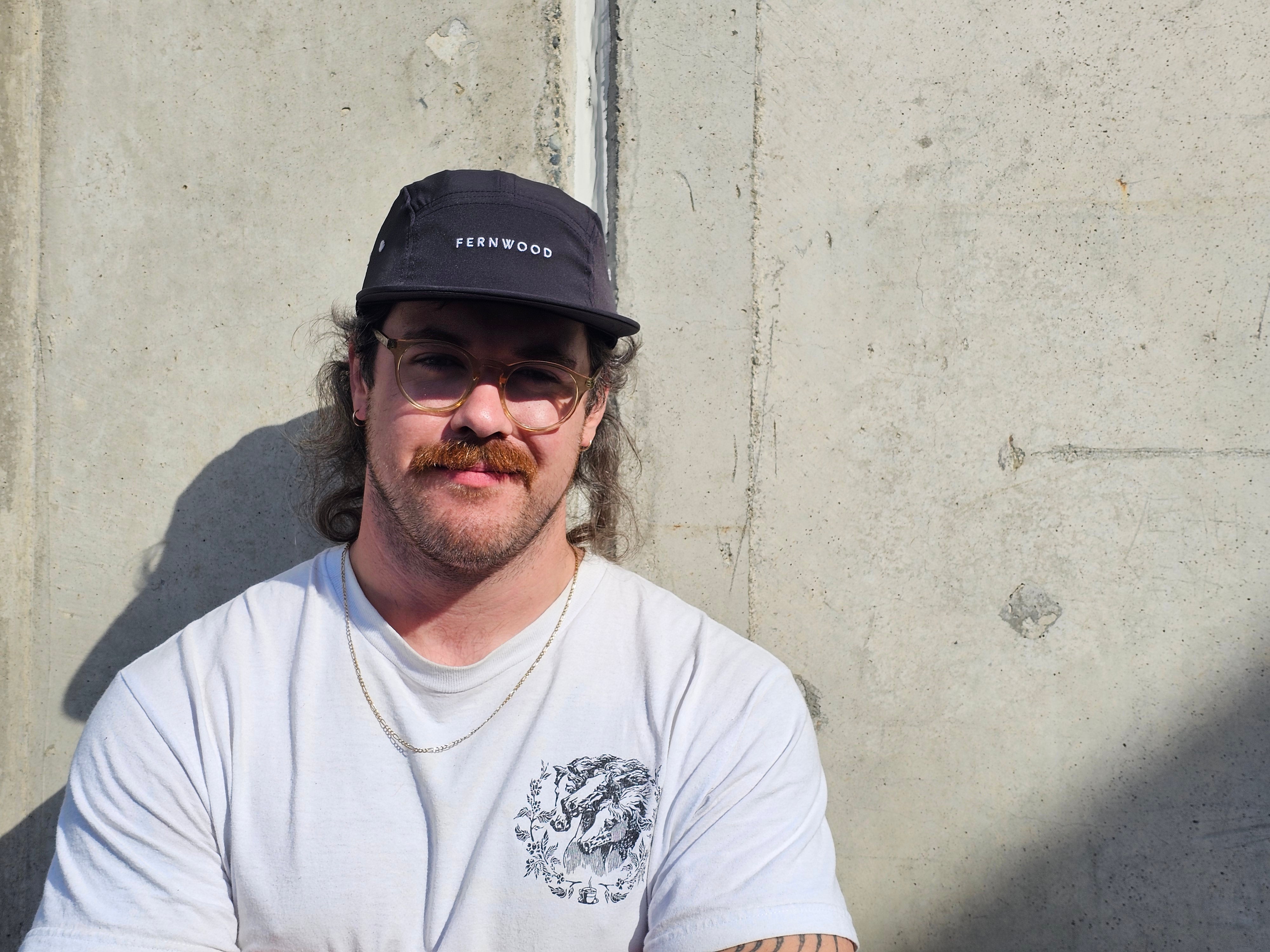 Man wearing a cap and white t-shirt with a logo against a concrete wall