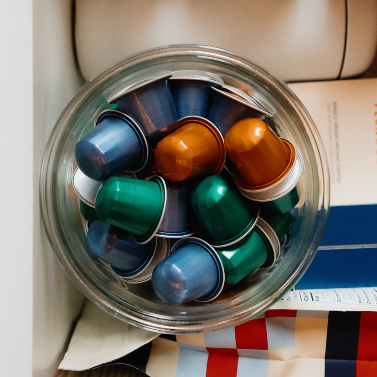 Glass jar filled with colorful coffee capsules in amessy coffee drawer.