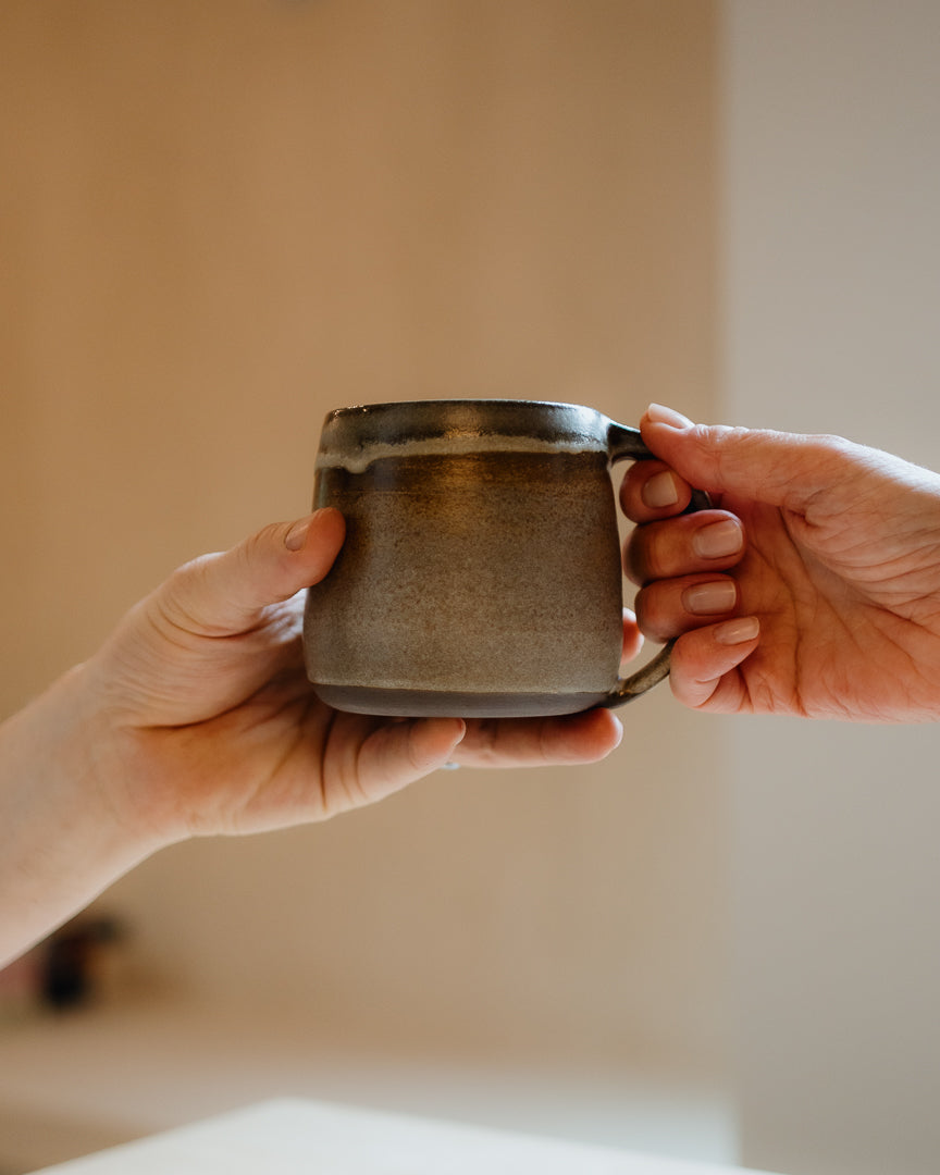 Two hands holding a ceramic mug against a neutral background