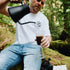 Man in a forest setting pouring coffee from a black coffee pot into a glass.