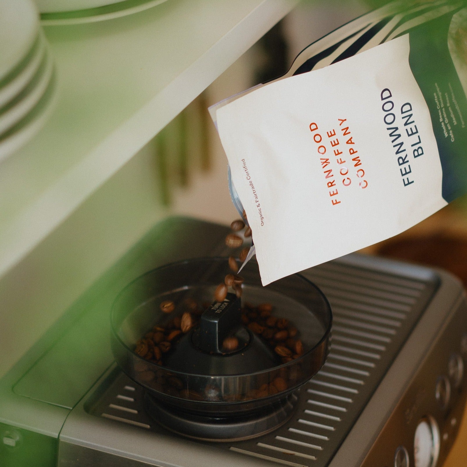 Coffee beans being poured into a grinder in top of an espresso machine in a kitchen.