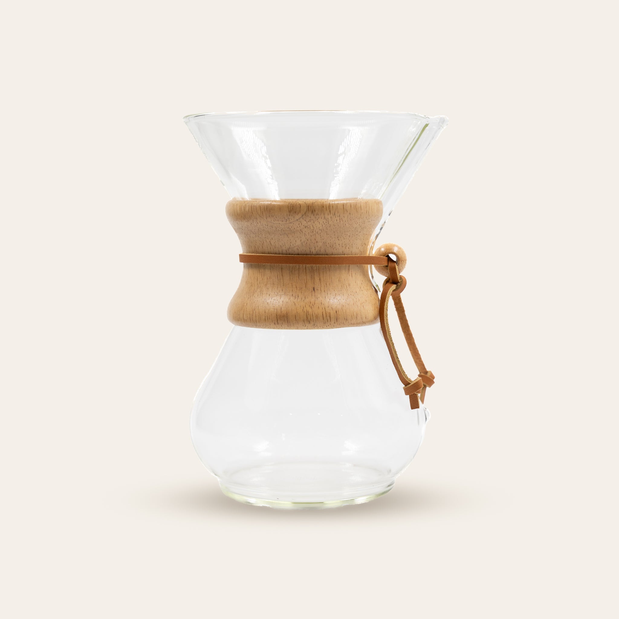 Chemex clear glass coffee maker with wooden collar on a beige background