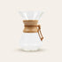 Chemex clear glass coffee maker with wooden collar on a beige background