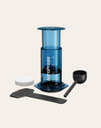Blue AeroPress coffee maker with accessories on a beige background