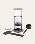 AeroPress coffee maker with components on a light beige background