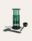 Green AeroPress coffee maker with components on a beige background