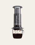 AeroPress coffee maker with coffee being brewed on a light beige background