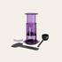 Purple AeroPress coffee maker with accessories on a beige background
