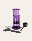 Purple AeroPress coffee maker with accessories on a beige background