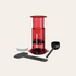Red AeroPress coffee maker with black scoop and white filter on a beige background
