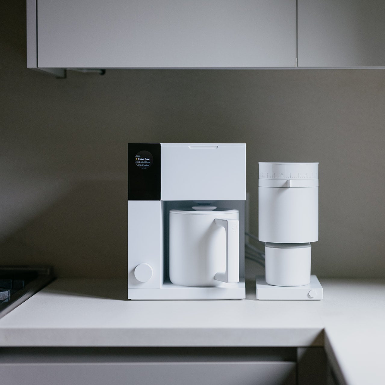 White coffee maker and grinder on a kitchen counter with a neutral background