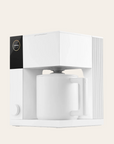 A matte white FELLOW Aiden Precision Coffee Maker with a single cup placed inside, set against a plain background.