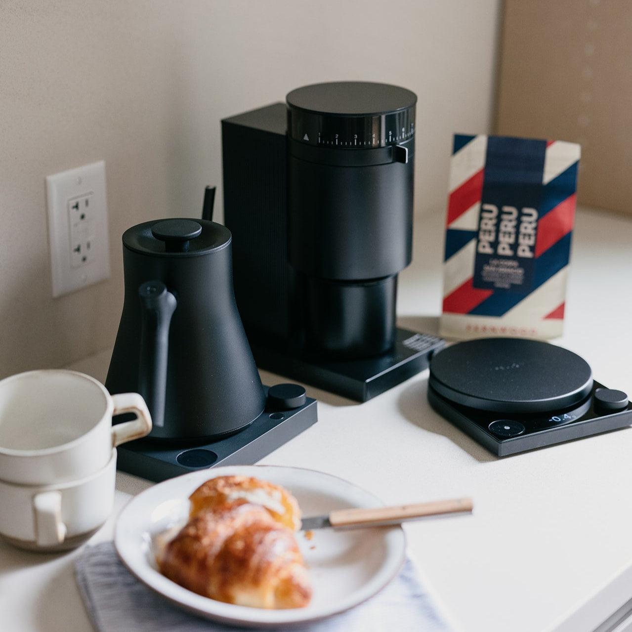 Black coffee maker on a kitchen counter with a croissant and coffee cup.