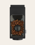 Black coffee grinder with coffee beans on a beige background