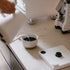Person pouring coffee from a white kettle into a white mug on a kitchen counter.