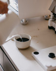 Person pouring coffee from a white kettle into a white mug on a kitchen counter.