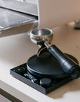 Coffee tamping device on a kitchen counter with a coffee machine in the background