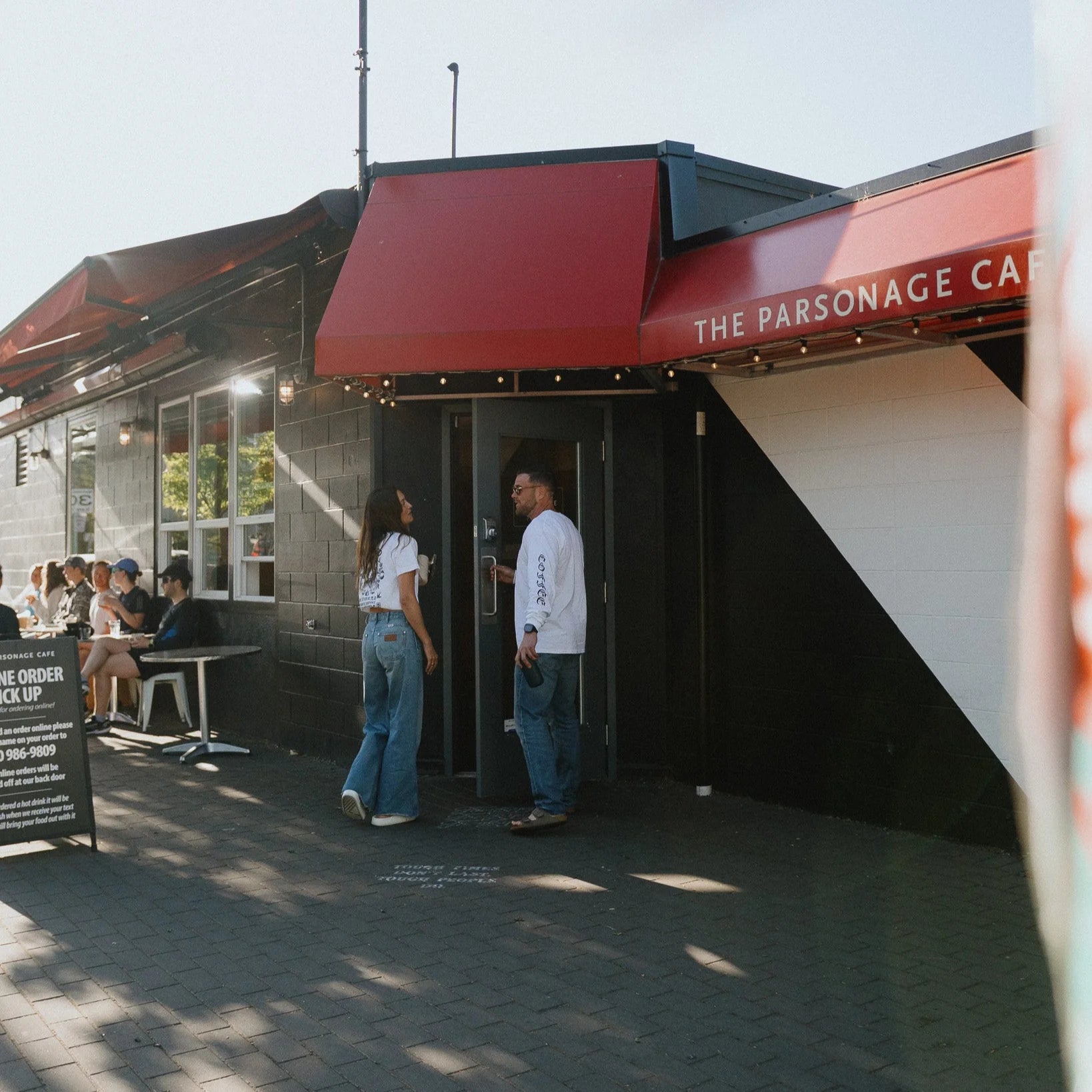 Two people standing outside a building with a red awning labeled 'The Parsonage Cafe'.