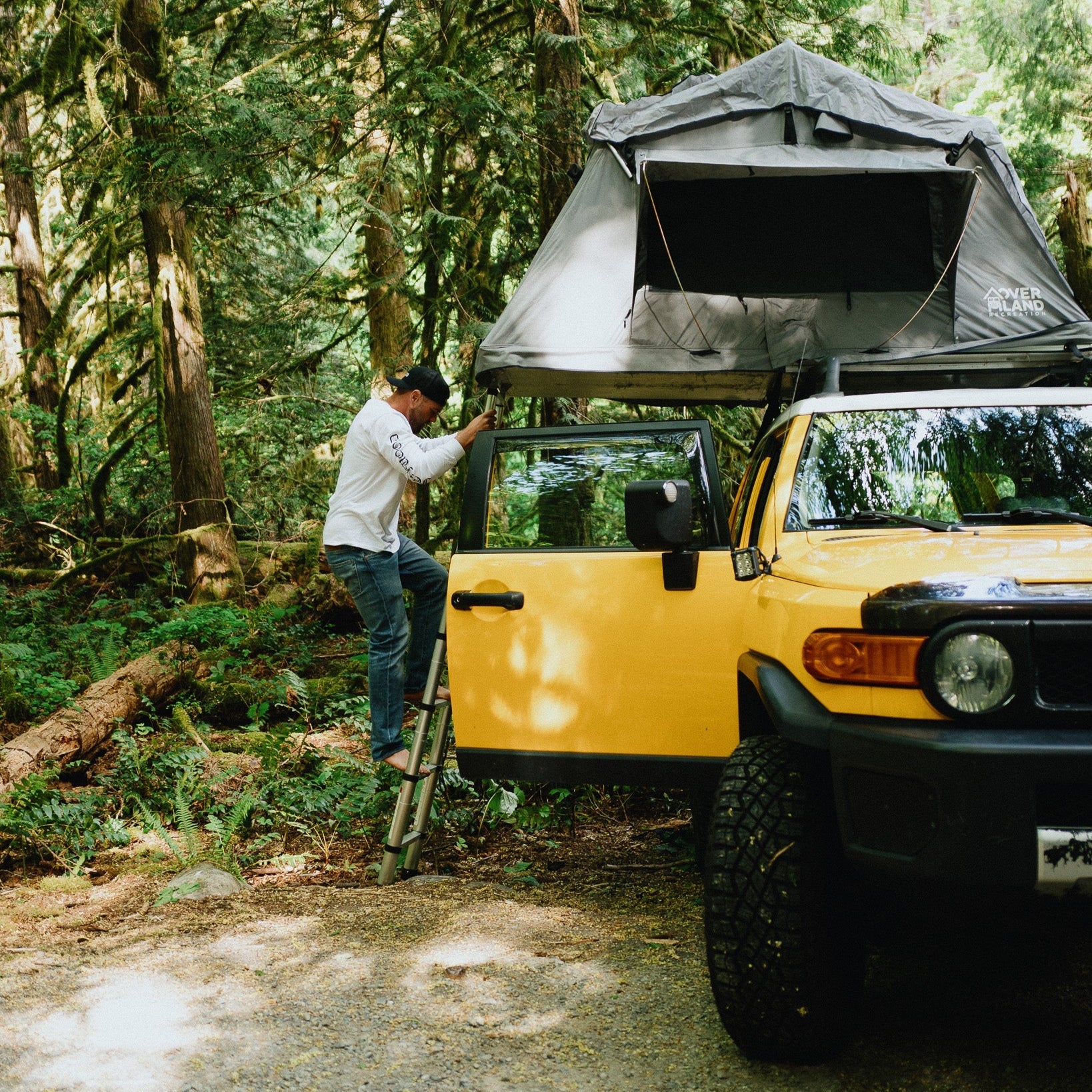 Person setting up a rooftop tent on a yellow SUV in a forest