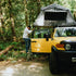 Person setting up a rooftop tent on a yellow SUV in a forest