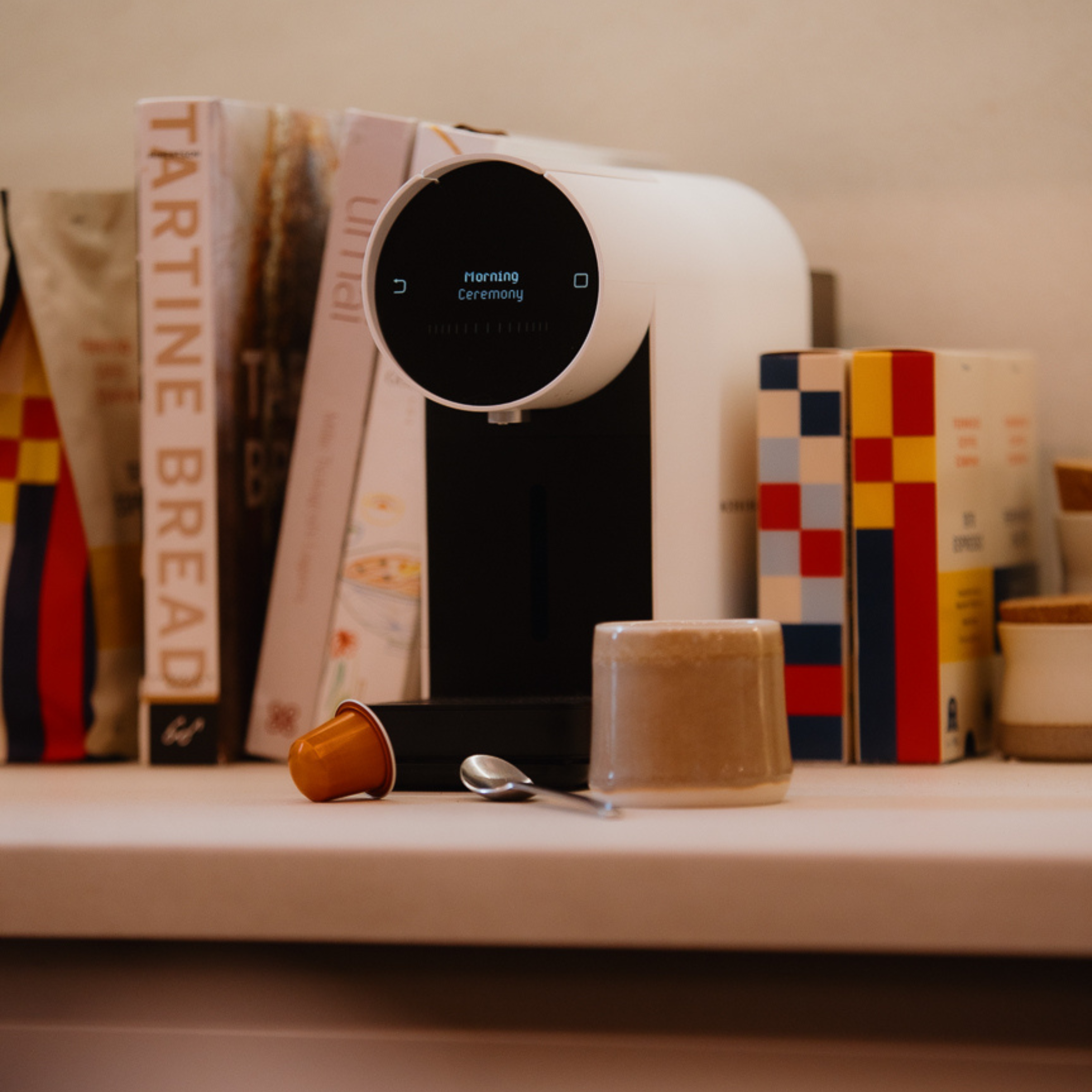 White coffee machine on a counter with books and a coffee pod in the foreground
