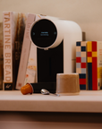 White coffee machine on a counter with books and a coffee pod in the foreground