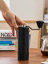 Hand on a black Nuttii Goosey hand grinder on a wooden desk