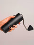 Hand holding a black Nuttii Goosey hand grinder sideways