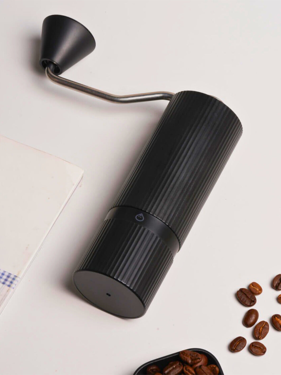 Black Nuttii Goosey hand grinder lying on its side next to coffee beans