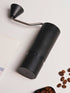 Black Nuttii Goosey hand grinder lying on its side next to coffee beans