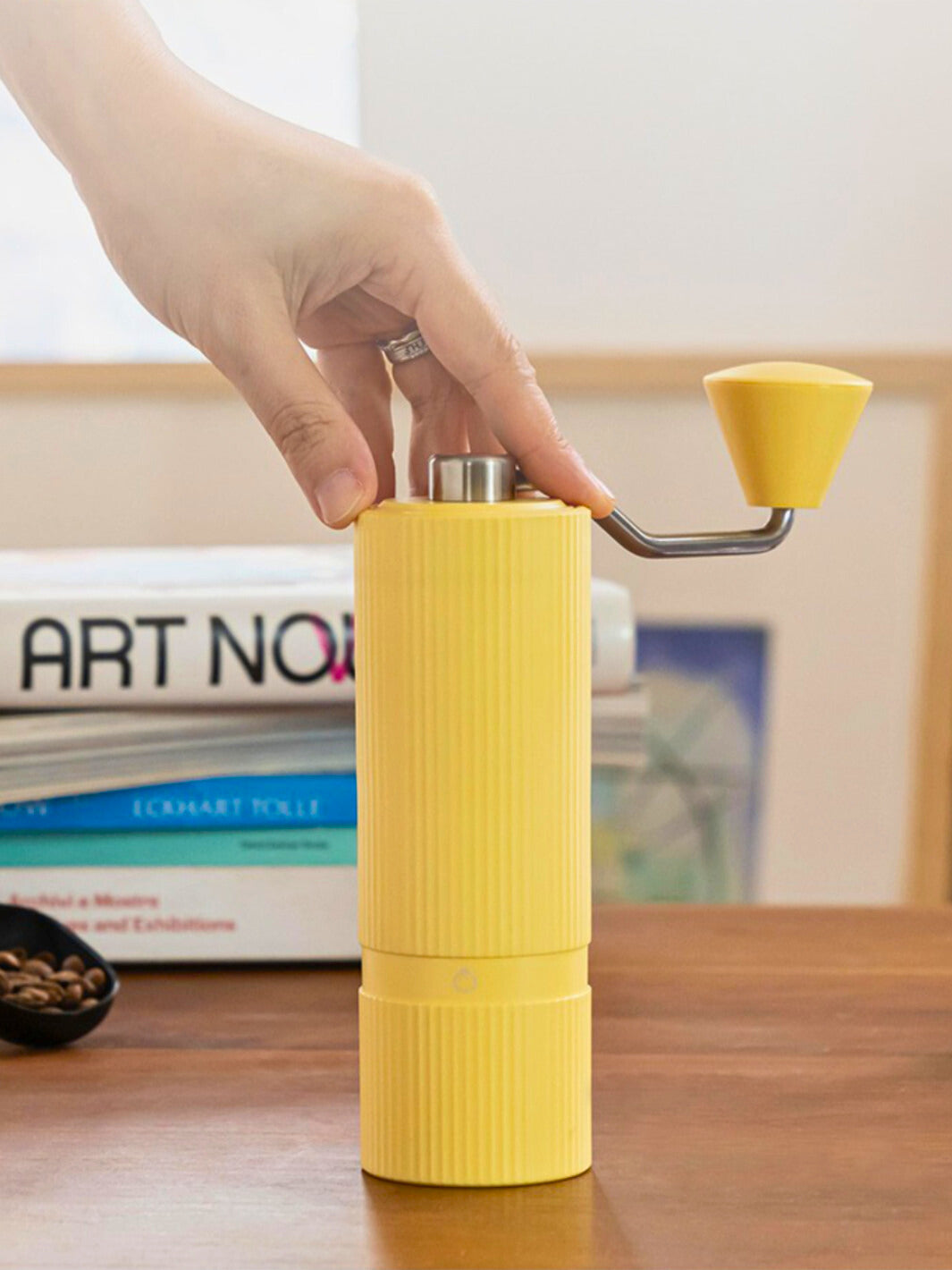 Hand turning a yellow Nuttii Goosey hand grinder on a wooden table with books
