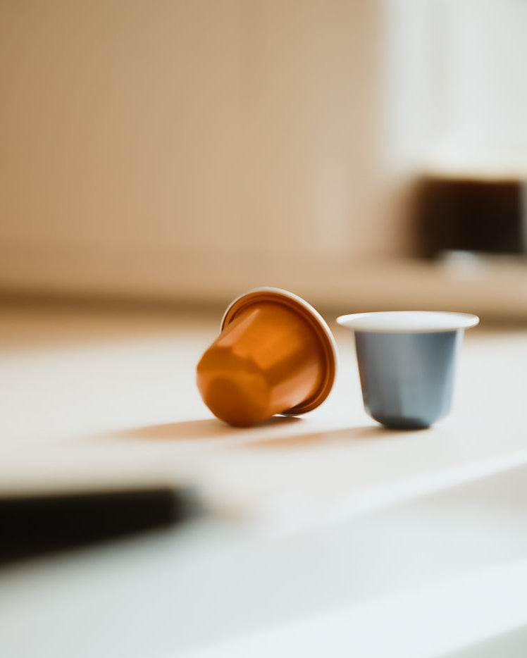 Two coffee capsules on a light surface with a blurred background