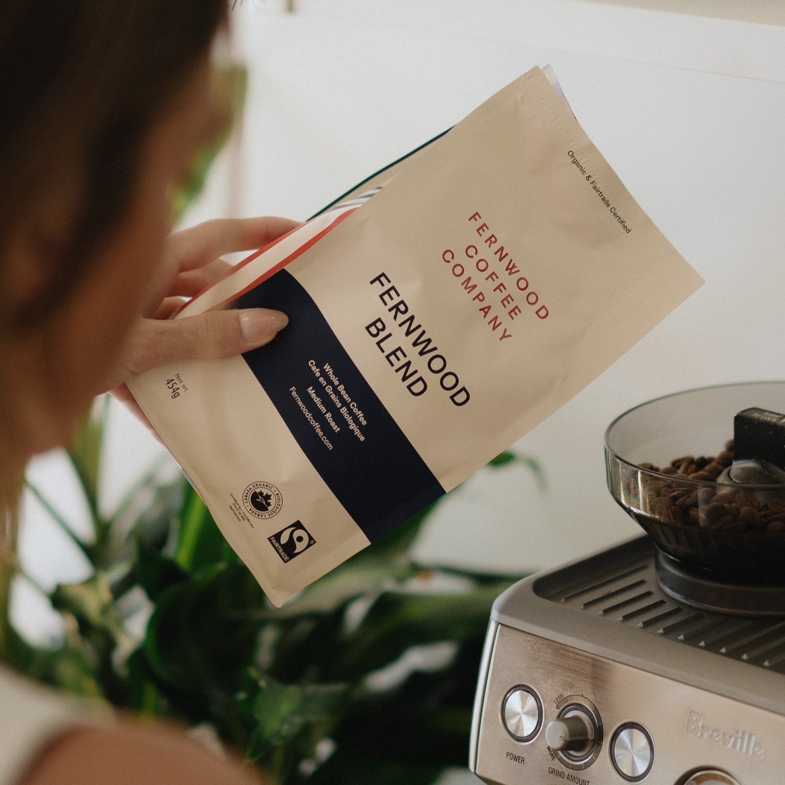 A person holding a bag of Fernwood Blend getting ready to pour beans into a grinder.