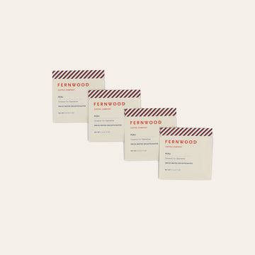 Four Fernwood coffee packages of Peru Decage instant on a beige background.
