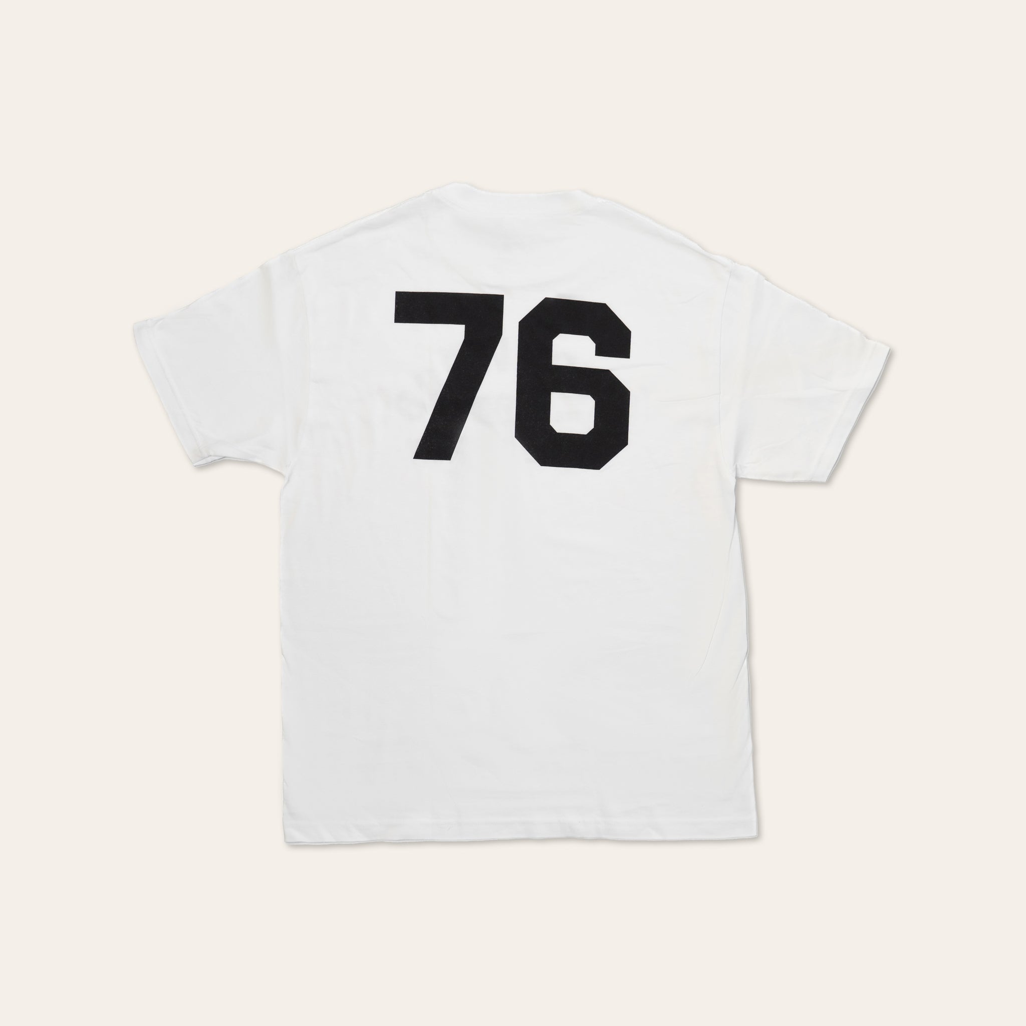 Back of a white tshirt with large 76 numbering in black on a beige background