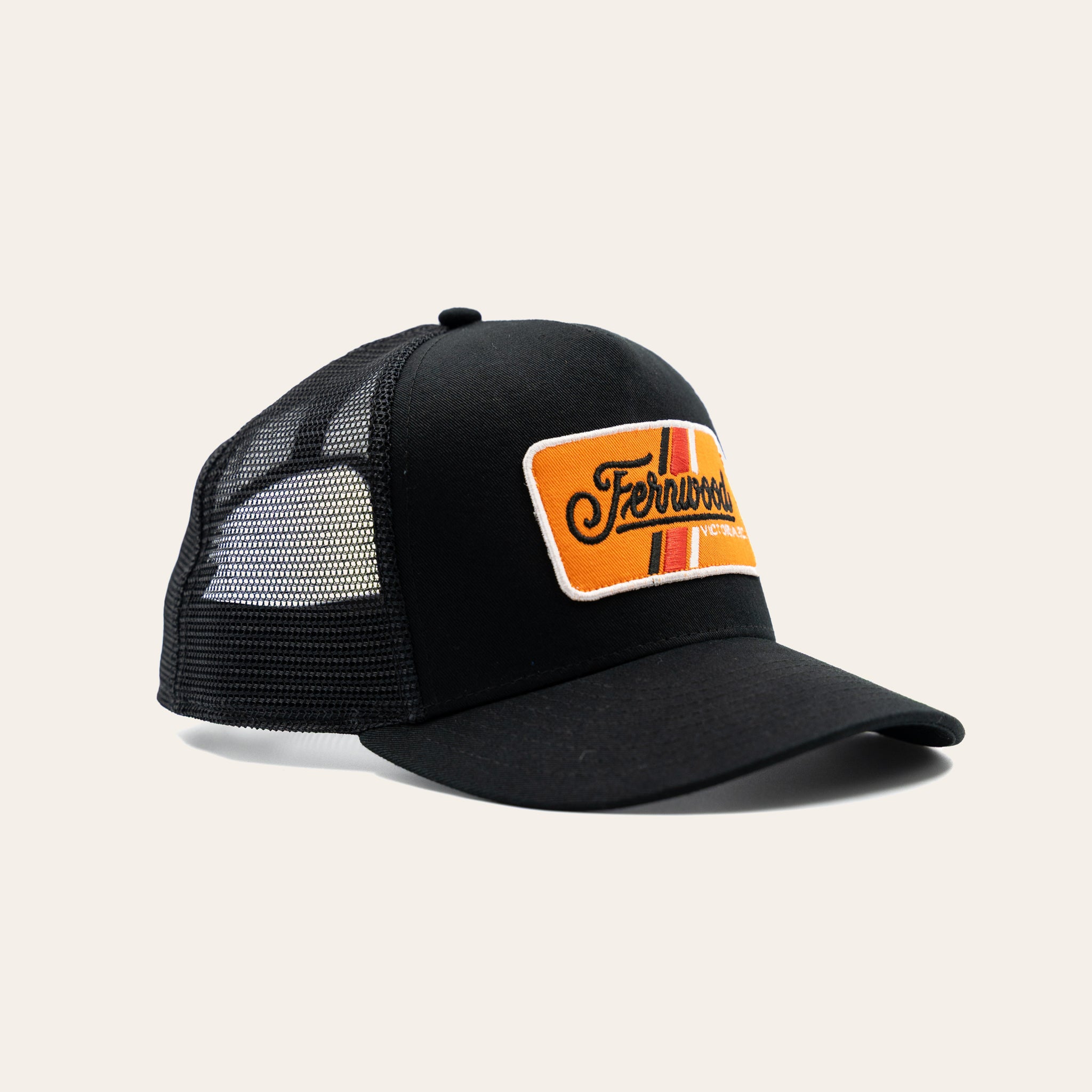 Black mesh cap with an orange and yellow Fernwood patch on a beige background