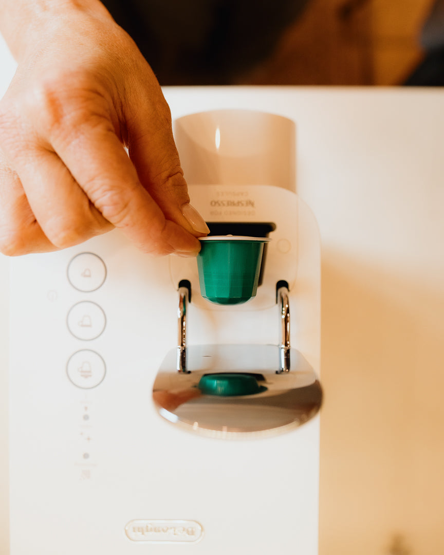 Hand inserting a green West Coast Trail coffee pod into a white Nespresso machine.