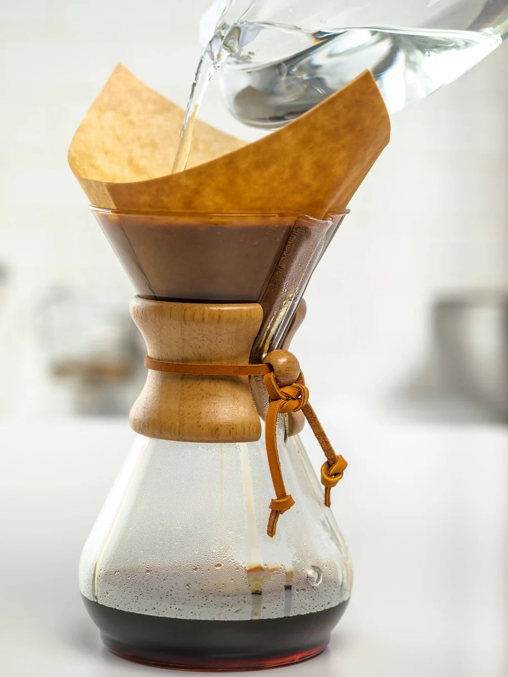 Glass Chemex coffee maker with wooden collar and filter on a beige background