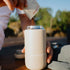 Person pouring instnat coffee into a beige thermos with 'FERNWOOD' branding, outdoors.