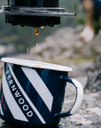 Coffee dripping from the bottom of an Aeropress brewer into a mug outdoors while camping.