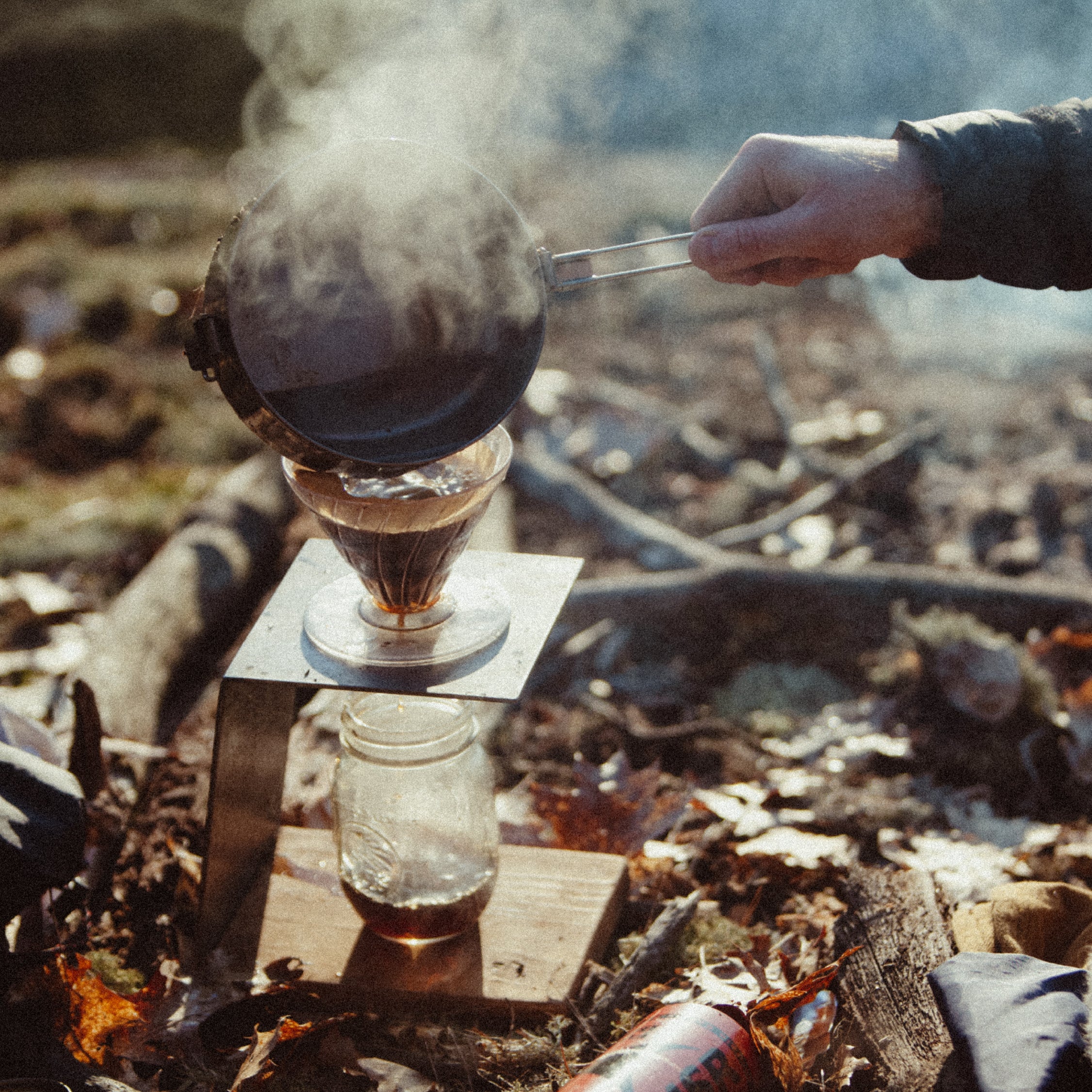 A person pouring boiling water into a Hario V60 maker while outdoors camping in the morning light