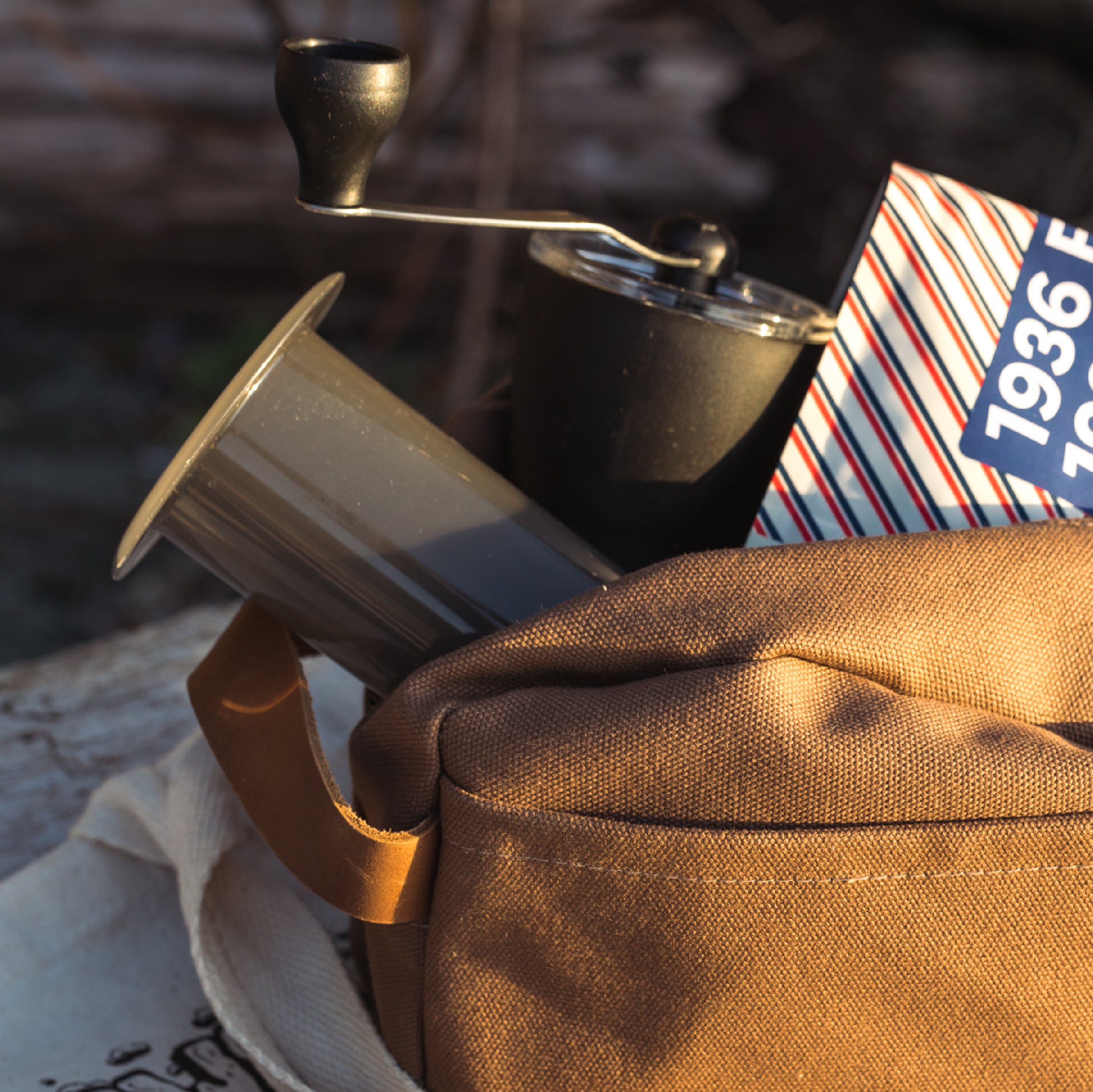 A backpack sitting outdoors with an Aeropress Brewer, Grinder and bag of coffee sticking out of the backpack.